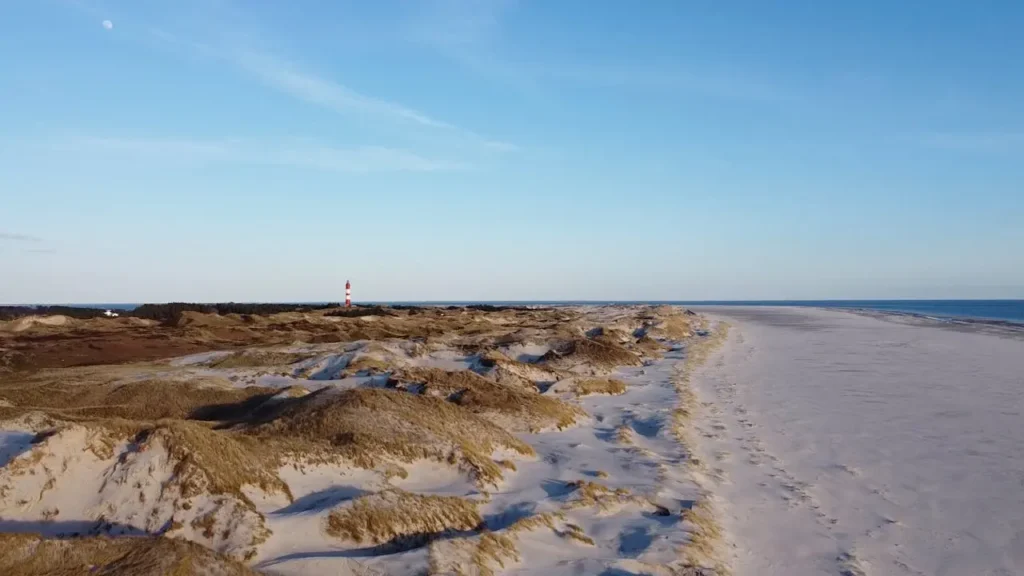Breiter Sandstrand mit Leuchtturm im Hintergrund